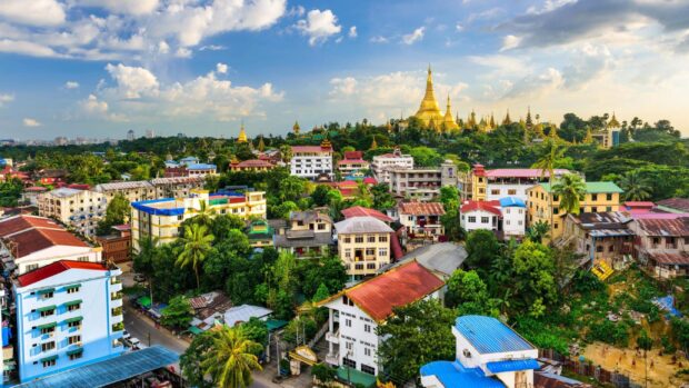 A panoramic view of Myanmar cityscape with a golden pagoda and lush greenery under a blue sky