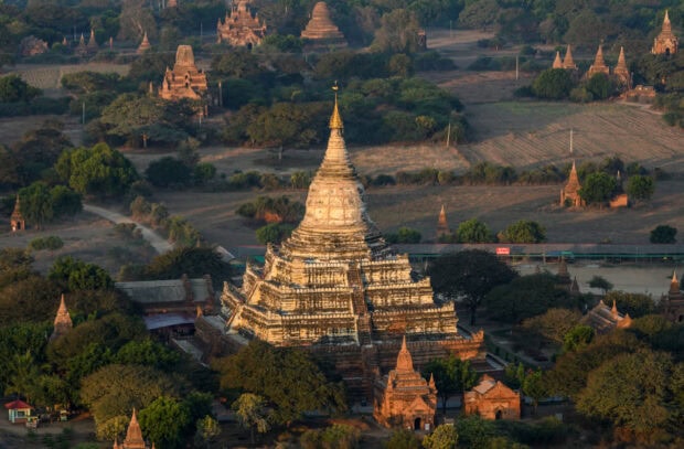 Ancient Myanmar temple ruins surrounded by trees and fields in a historic site