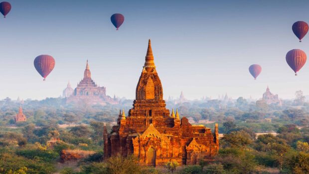 Ancient Myanmar temple with hot air balloons flying over lush landscape at sunrise