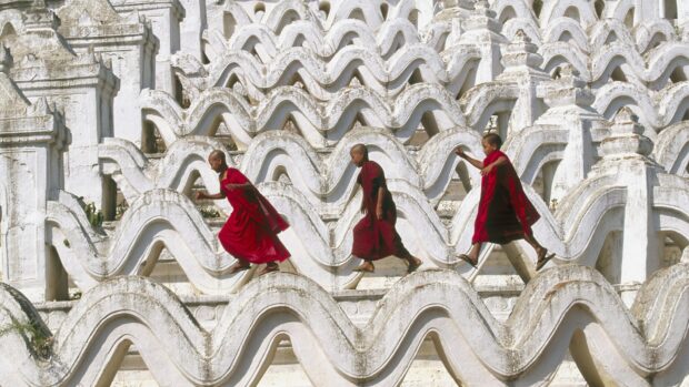 Three young monks walking on the white curved architecture at a historic Myanmar site