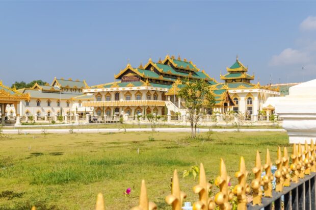 Traditional Myanmar architecture with golden roofs under clear blue sky in a green field