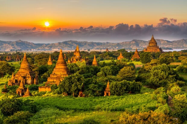 Ancient Myanmar temples surrounded by lush green fields under a sunset sky