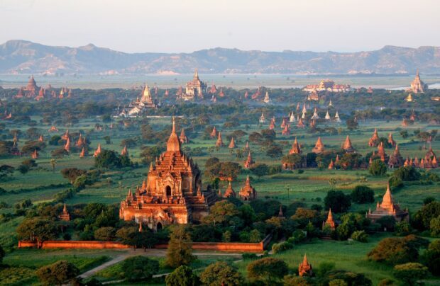 Ancient temples and pagodas in Myanmar landscape during sunrise with green fields and hills in the background