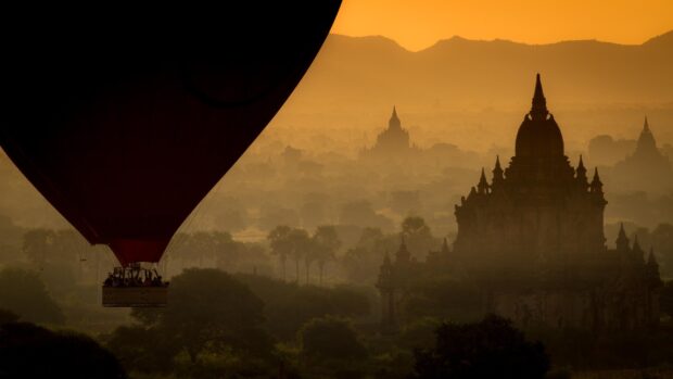 A hot air balloon flying over ancient temples and lush trees in Myanmar at sunrise