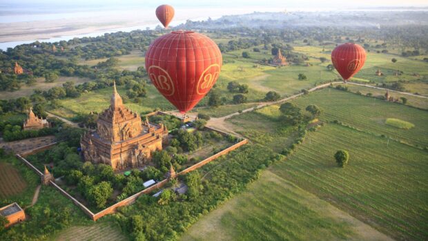 Hot air balloons flying over ancient temples in Myanmar landscape with greenery and fields