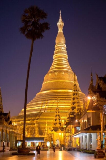 Golden pagoda in Myanmar at night with people walking nearby