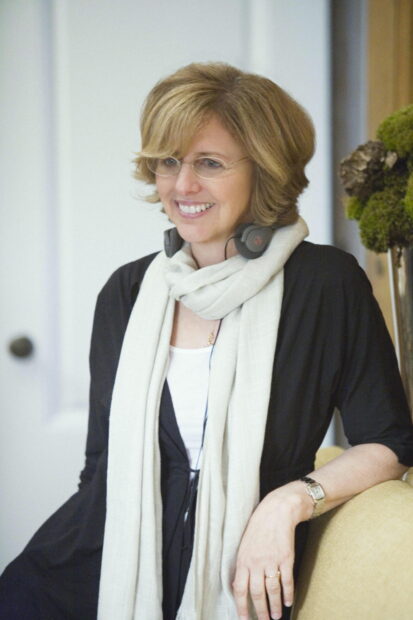 Nancy Meyers wearing glasses and a scarf smiling indoors