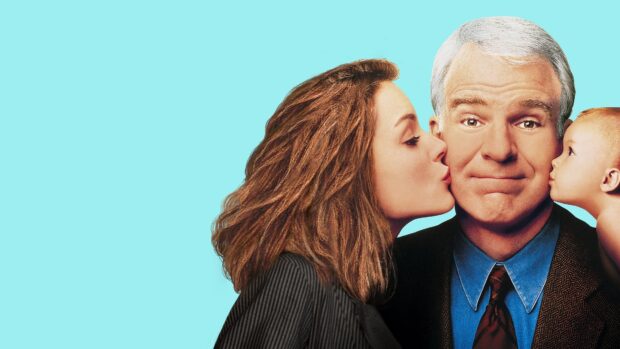 A middle aged man receiving kisses from a woman and a baby on his cheeks against a blue background