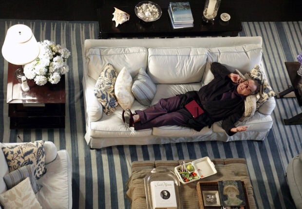 A man resting on a white couch surrounded by decorative pillows in a cozy living room setting
