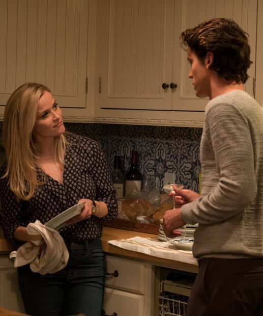 A woman drying a dish while talking to a man holding a glass in a kitchen setting