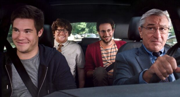 Four men smiling and driving in a car with comedic expressions showing friendship and humor
