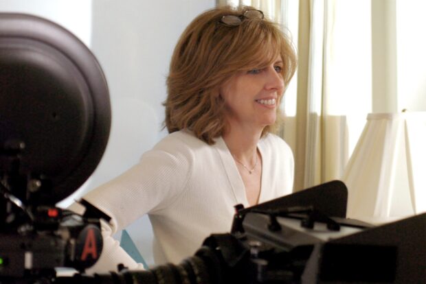 Nancy Meyers smiling while working on a film set with camera equipment visible
