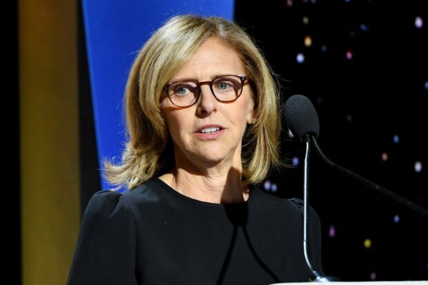 Nancy Meyers speaking at an event with a microphone wearing glasses and a black dress