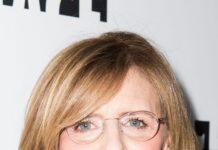 Nancy Meyers wearing glasses and black jacket with a bright smile in a close up portrait