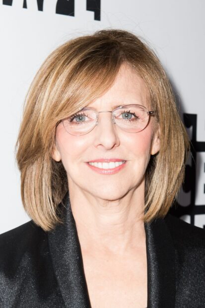 Nancy Meyers wearing glasses and black jacket with a bright smile in a close up portrait
