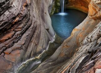 Curved rock formations surround a waterfall and pool in a natural geological formation