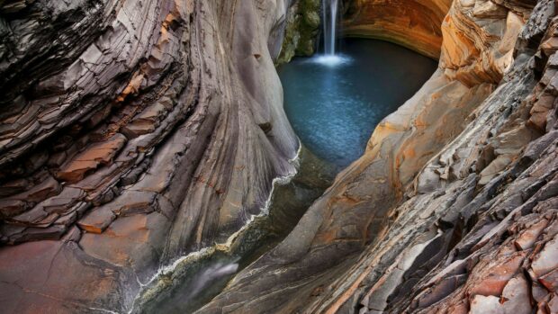 Curved rock formations surround a waterfall and pool in a natural geological formation