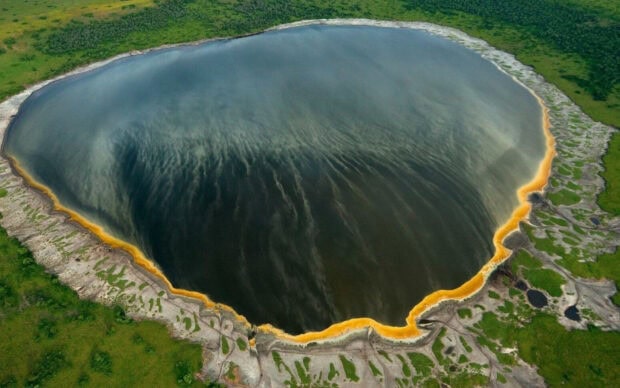 Aerial view of volcanic crater lake with orange rim and surrounding green landscape captured by National Geographic