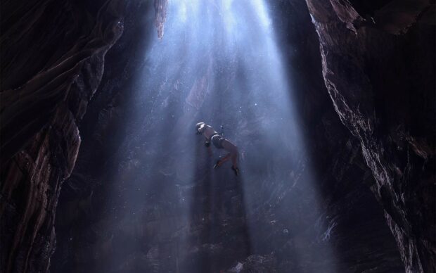A person descending into a deep cave illuminated by natural light from above in a National Geographic adventure