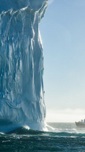 A massive iceberg towering over the ocean near a boat in a National Geographic landscape