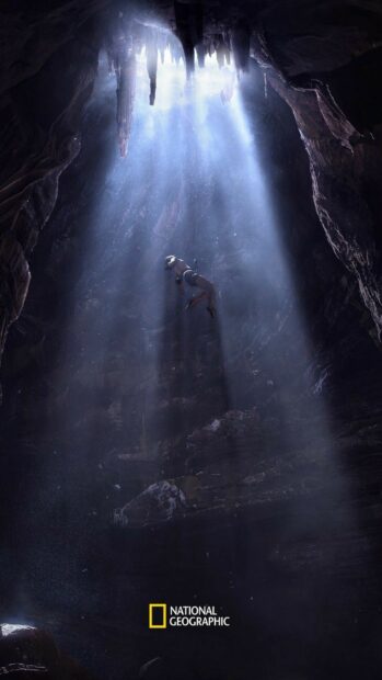 A person exploring a deep cave with sunlight shining through cracks National Geographic