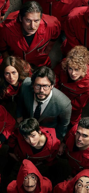 The cast of the Netflix series wearing red jumpsuits and looking up together