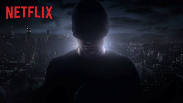 Daredevil from Netflix stands in front of a dark cityscape at night with a glowing light behind him