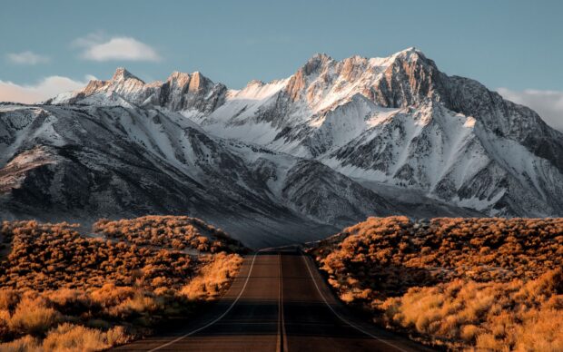 A scenic view of Nevada mountains with snow covered peaks and a road leading through autumn colored shrubs