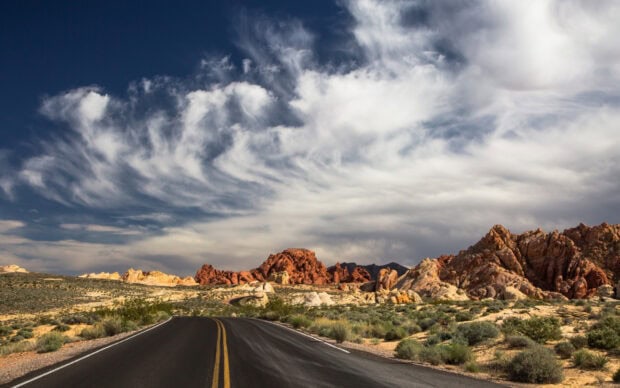 Winding road through Nevada desert with red rocks and cloudy sky