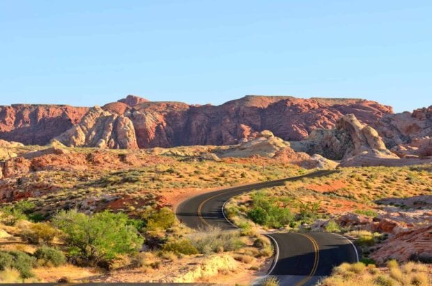 Winding road passing through Nevada desert with red rock formations and clear sky