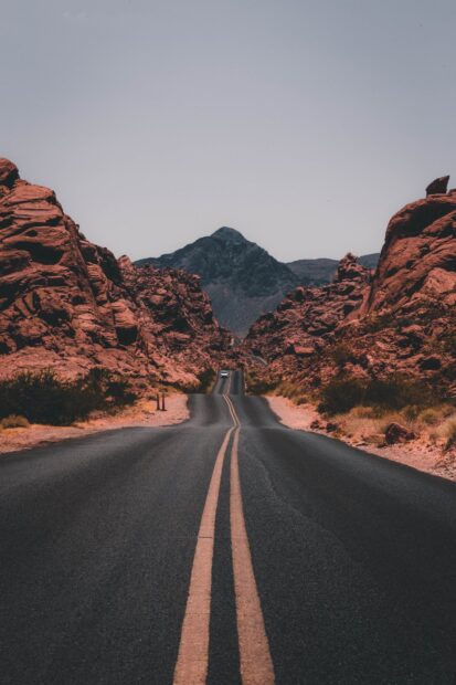 A scenic road leading through rocky desert mountains in Nevada with clear sky and distant peak