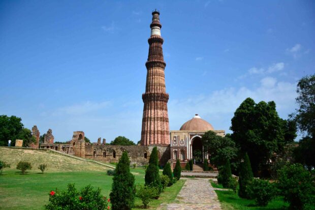 Qutb Minar tower in New Delhi with historic ruins and greenery under a clear sky