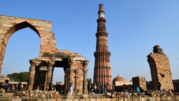 The Qutub Minar and ancient ruins in New Delhi with clear blue sky and tourists