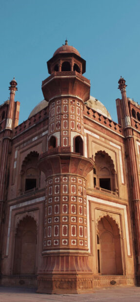 Historic New Delhi architecture with detailed red sandstone tower and blue sky background