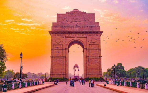 The India Gate monument at sunset with people and birds in New Delhi cityscape