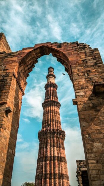Qutub Minar framed by ancient stone arch in New Delhi sky