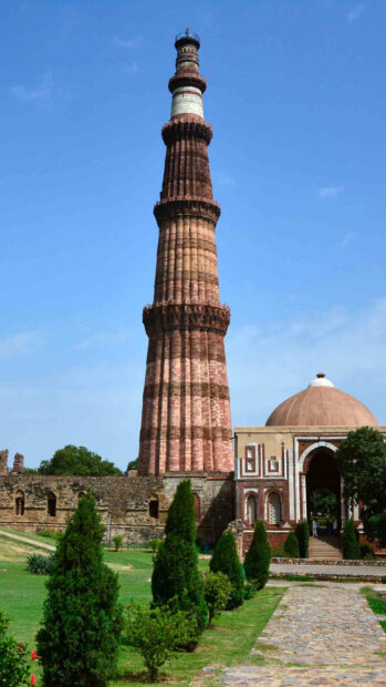 Historic Qutub Minar tower in New Delhi surrounded by greenery and clear sky