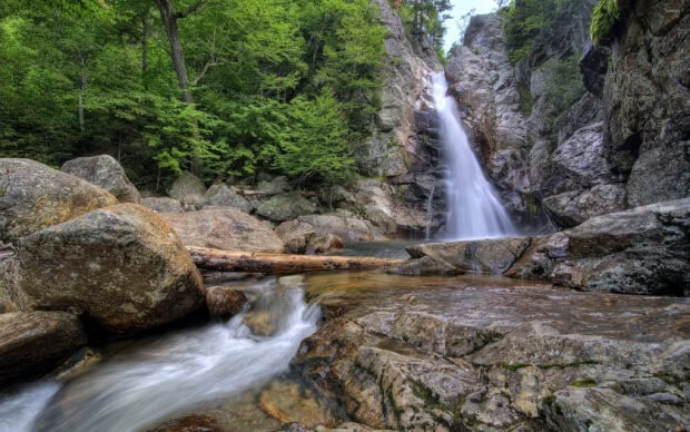 A serene waterfall surrounded by rocks and lush green trees in New Hampshire forest