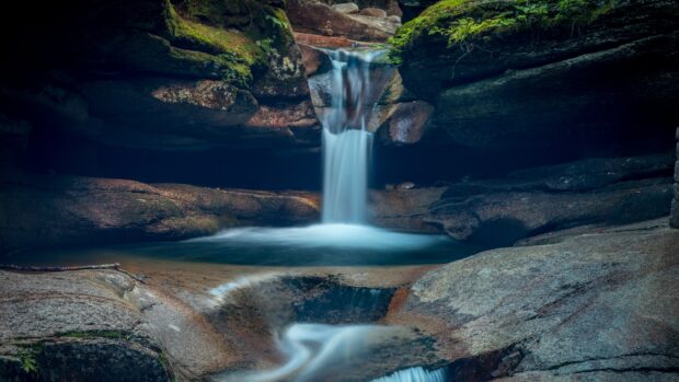 A serene New Hampshire waterfall flowing through rocky terrain with lush green moss