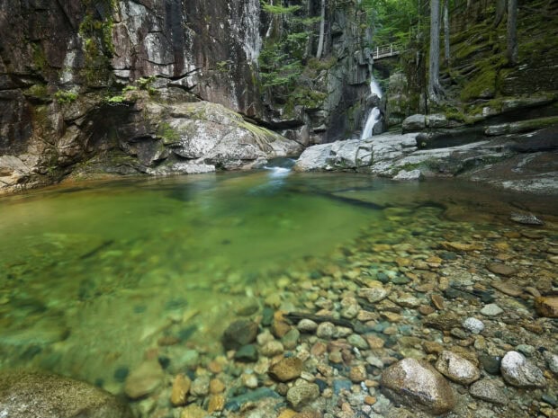 Clear green water pool with rocks and a small waterfall in New Hampshire