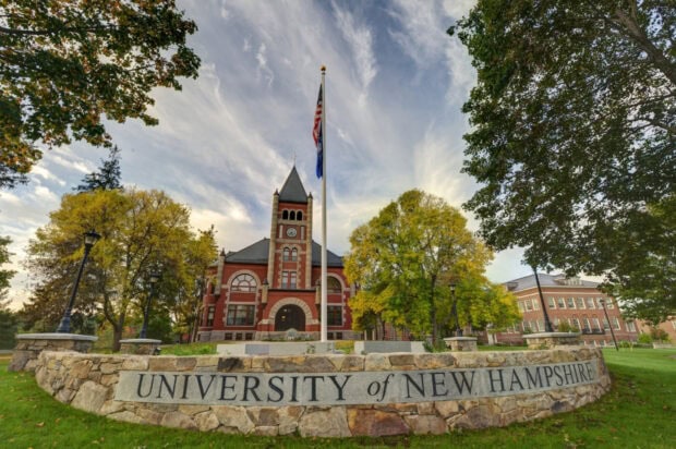 The University of New Hampshire building with trees and flagpole in clear sky during autumn