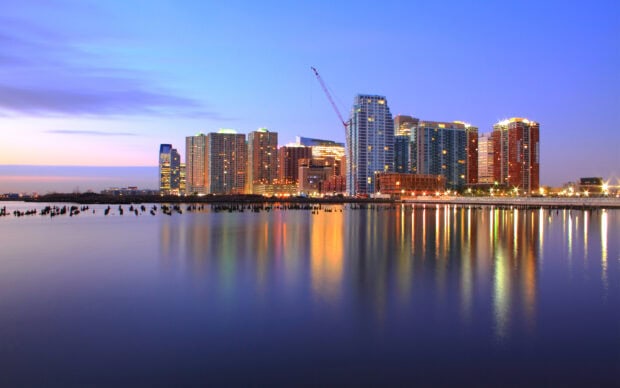 A beautiful cityscape of New Jersey with illuminated buildings reflecting on calm water at dusk
