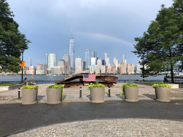A scenic view of New Jersey skyline with a rainbow over the city and an American flag in the foreground