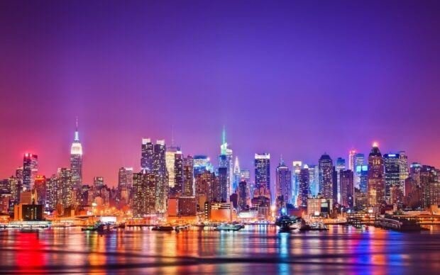 New York city skyline at night with vibrant lights and colorful reflections on the water