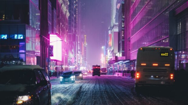 Snow covered street with New York signs and vehicles at night in the city