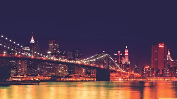 New York city skyline at night with illuminated buildings and Brooklyn bridge lights reflecting on the river