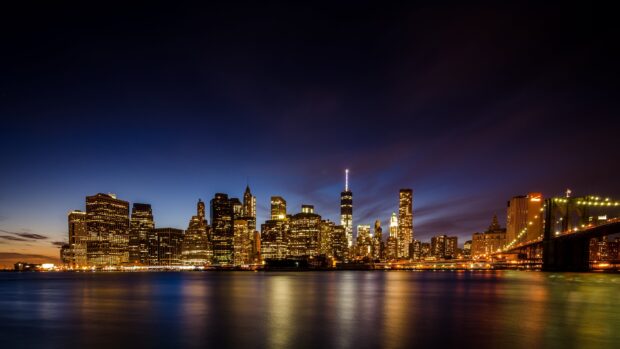 New York city skyline at night with illuminated buildings and calm river reflections