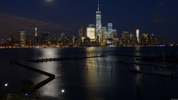 New York city skyline at night with illuminated buildings reflecting over calm river