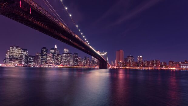 New York city skyline with bridge lights reflecting on water at night