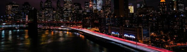 New York cityscape at night with skyscrapers and illuminated traffic trails on the bridge